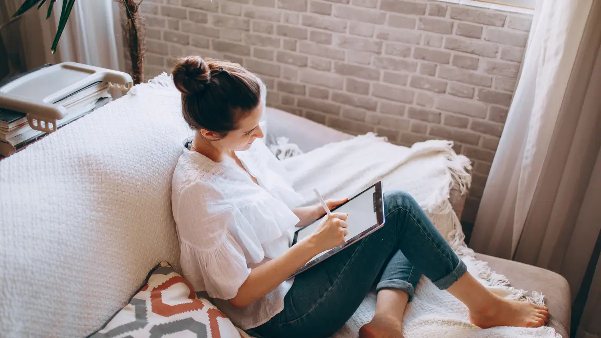 Femme allongée dans un canapé, une tablette sur les genoux