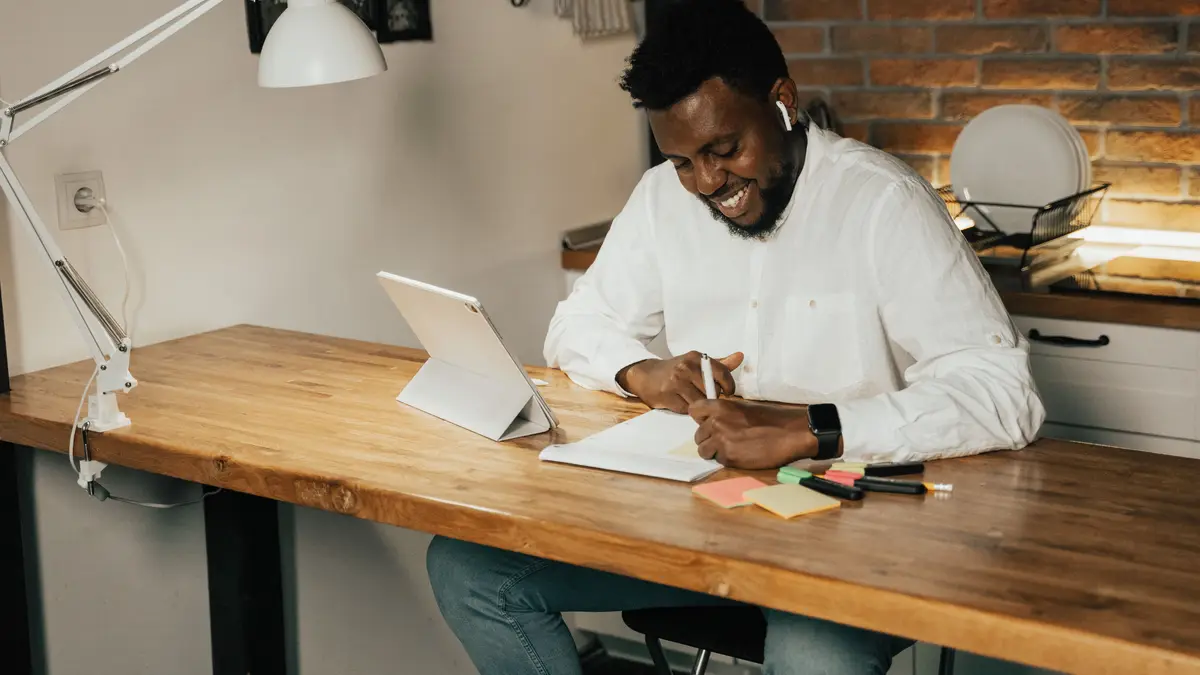 Étudiant souriant à son bureau, tablette sur support et carnet de notes