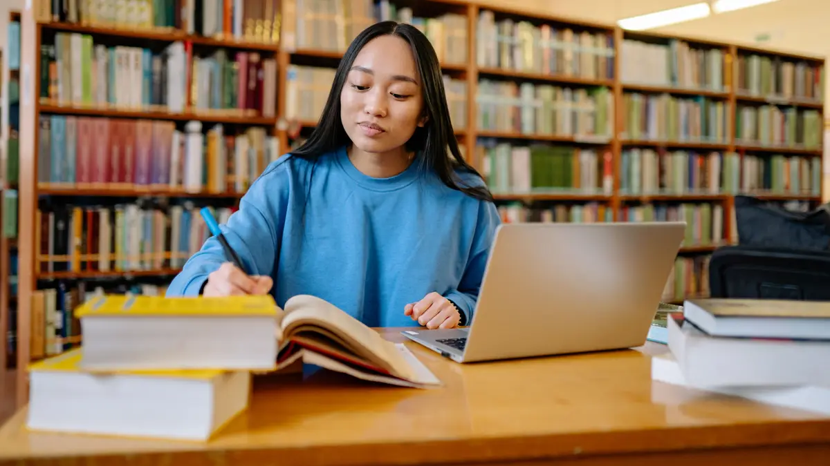 Étudiante en bibliothèque, entre ses livres et son ordinateur portable