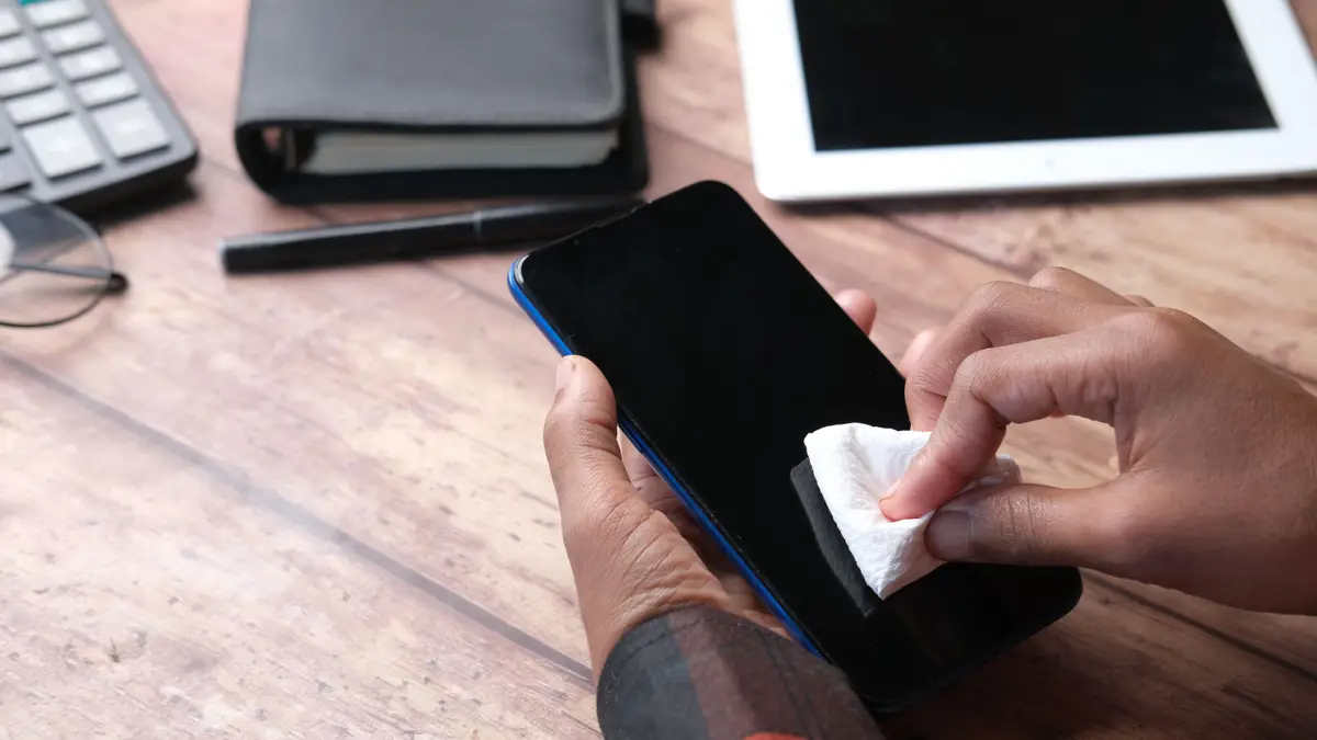 Nettoyage de l'écran d'un téléphone avec une lingette, une tablette à côté