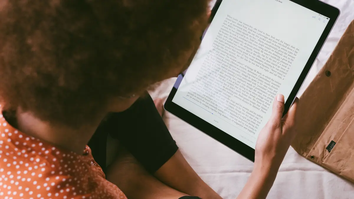 Personne lisant un texte sur une tablette, vue par-dessus l'épaule