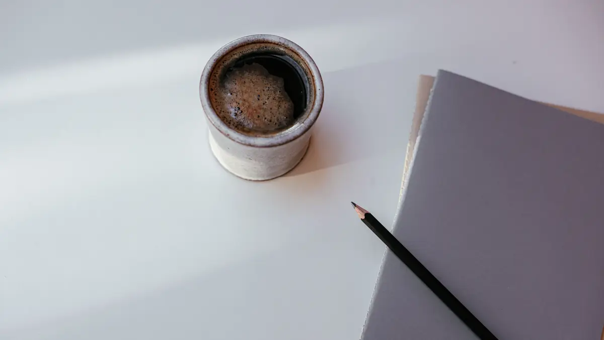 Carnet gris et crayon posés à côté d'une tasse de café