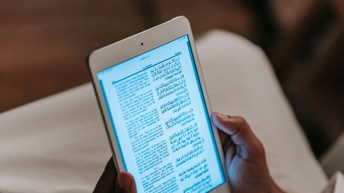 Mains tenant une petite tablette blanche ouverte sur un livre numérique