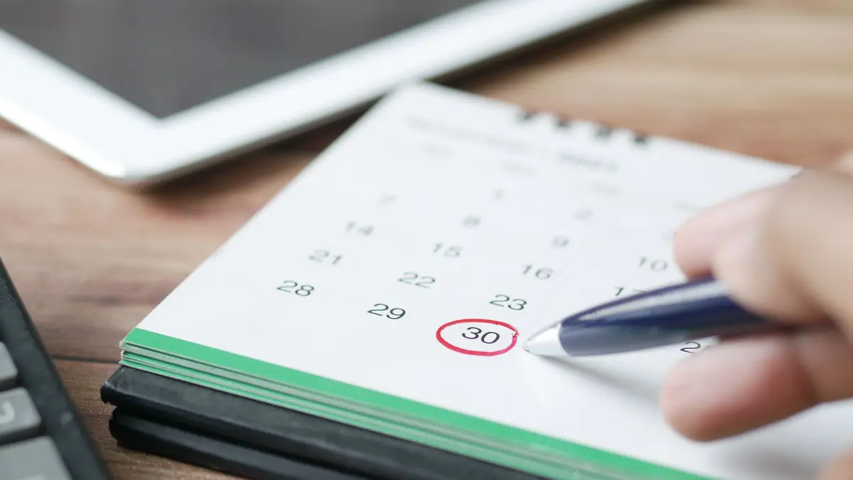 Stylo entourant une date sur un calendrier de bureau, une tablette à côté