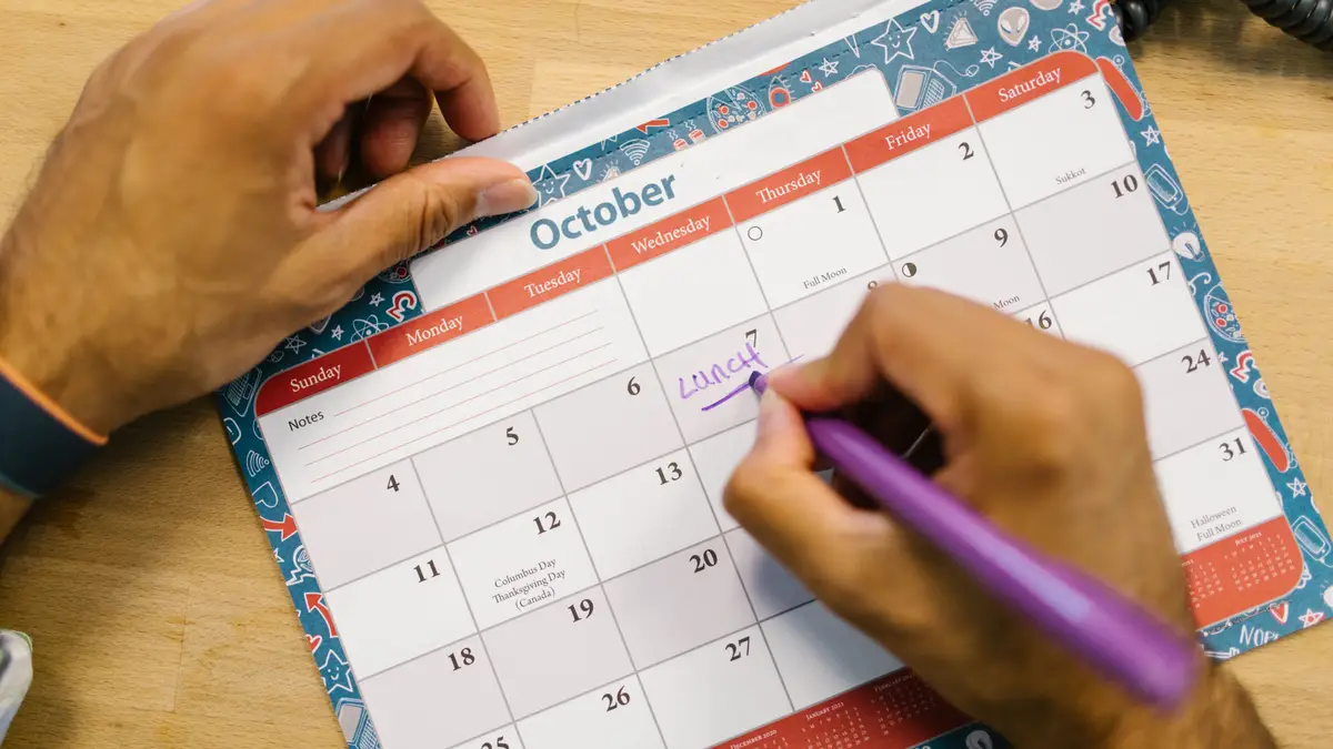 Main notant une date sur un calendrier mural ouvert au mois d'octobre
